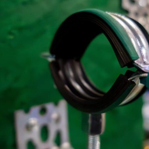 A green and black pipe anchor features a double-screw clamp. It stands on a screw against a green background.